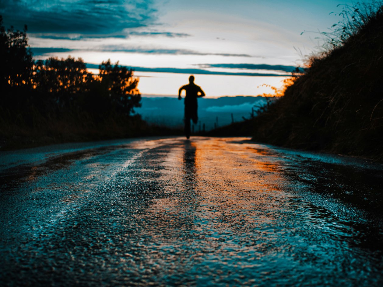 Runner silhouetted on a wet road at dusk